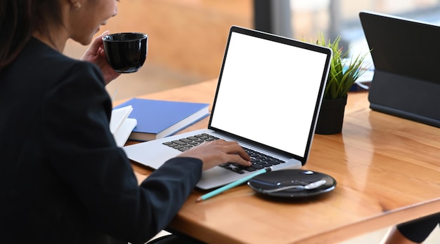 Ritagliata colpo di giovane donna d'affari che beve caffè e lavora su tablet computer alla scrivania dell'ufficio.