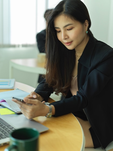 Ritagliata colpo di imprenditrice utilizza lo smartphone mentre era seduto al posto di lavoro