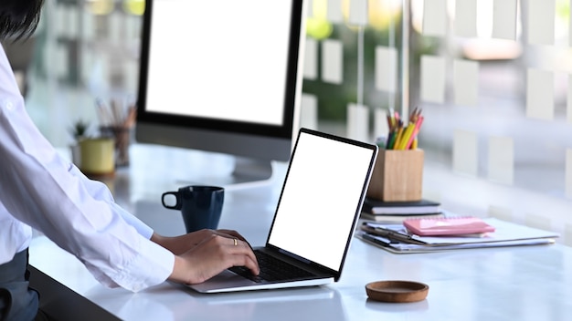 Ritagliata colpo di mani di impiegato di giovane donna digitando sulla tastiera del computer portatile sul posto di lavoro moderno.