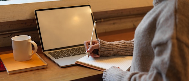 Ritagliata colpo di studentessa universitaria che fa i compiti con mock up laptop sul bancone bar in cafa