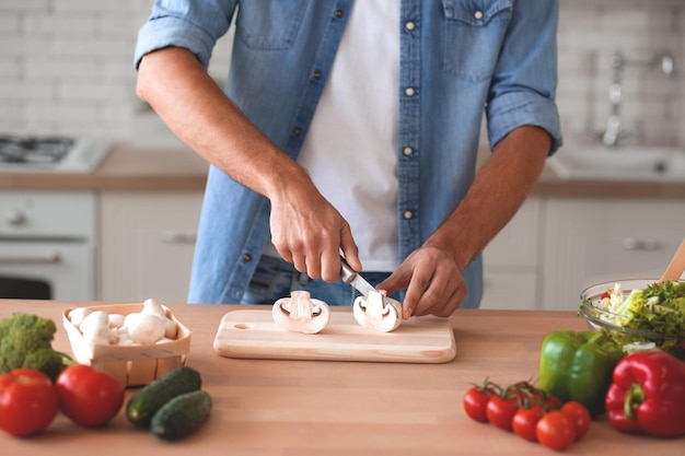 Ritagliata colpo di uomo che taglia i funghi sul tagliere in cucina