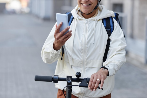 Ritagliata di un lavoratore sorridente che consegna il cibo che indossa il casco mentre guida uno scooter elettrico