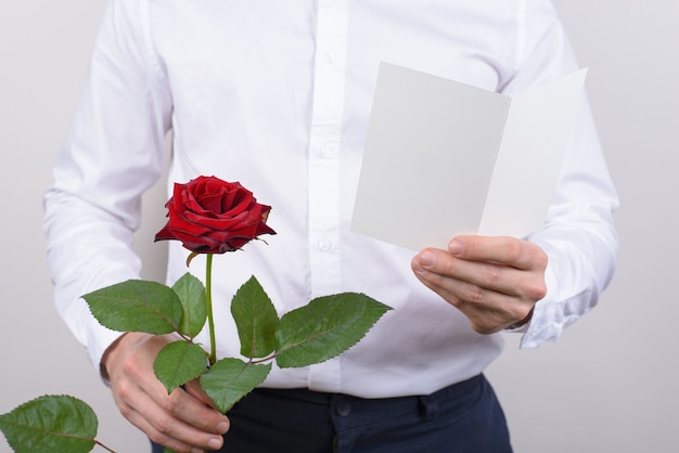 Ritagliata foto ravvicinata di allegro bello sorridente sincero innamorarsi ragazzo che apre il suo cuore all'amata signora leggendo poesia in possesso di carta cartolina in mani isolato sfondo grigio