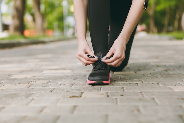 Ritagliato primo piano delle mani della donna che legano i lacci delle scarpe su scarpe da ginnastica nere e rosa durante il jogging o l'allenamento sul percorso all'aperto