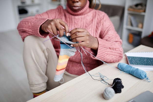 Ritagliato ritratto di giovane donna afroamericana che lavora a maglia a casa nello spazio della copia della stanza accogliente