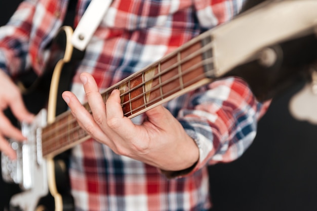 Ritagliato Ritratto di uomo vestito di camicia in una gabbia in piedi sulla lavagna mentre suona la chitarra.