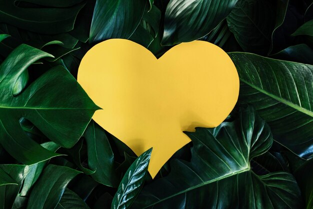 Ritaglio a forma di cuore giallo con foglie verdi Posa concetto di amore