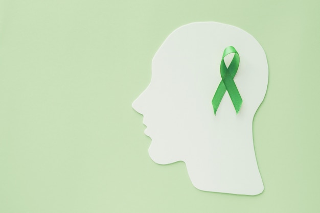 Ritaglio di carta del cervello con il nastro verde su fondo verde, concetto di salute mentale, giornata mondiale della salute mentale