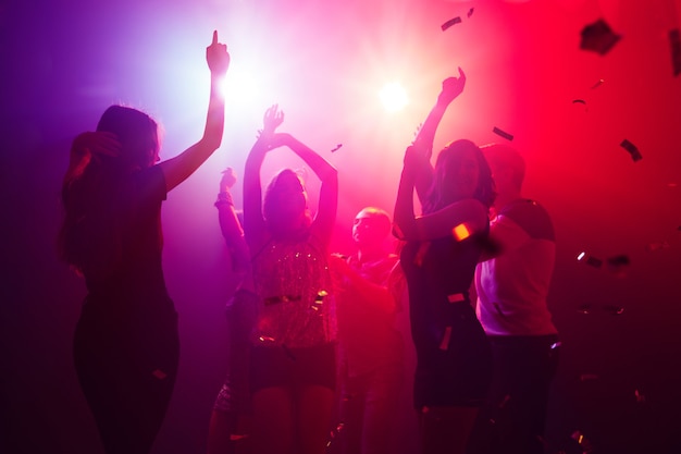 Ritmo. Una folla di persone in silhouette alza le mani sulla pista da ballo su sfondo di luce al neon. Vita notturna, club, musica, danza, movimento, gioventù. Colori viola-rosa e ragazze e ragazzi commoventi.