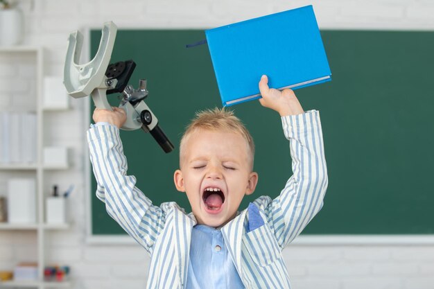 Ritorno a scuola eccitato allievo scolaro con microscopio e libro faccia buffa del piccolo studente di prim