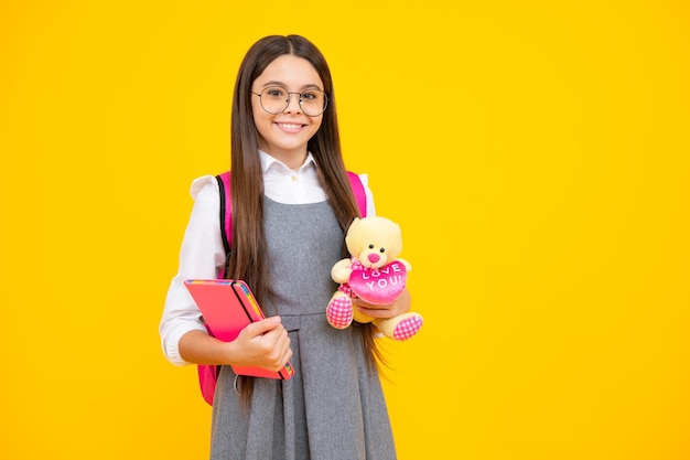 Ritorno a scuola La studentessa adolescente tiene il giocattolo Bambini della scuola con i giocattoli preferiti su sfondo giallo isolato dello studio