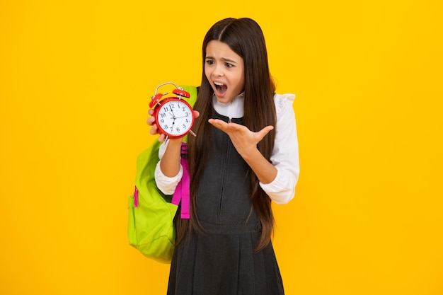 Ritorno a scuola Ragazza adolescente con borsa tenere orologio sveglia per imparare Scolara su sfondo giallo isolato Ragazza adolescente arrabbiata sconvolta e infelice emozione negativa