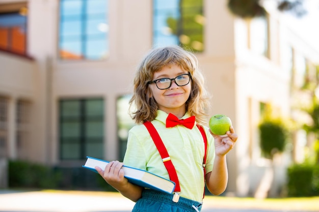 Ritorno a scuola ragazzino divertente con gli occhiali a scuola bambino della scuola elementare con libro e borsa