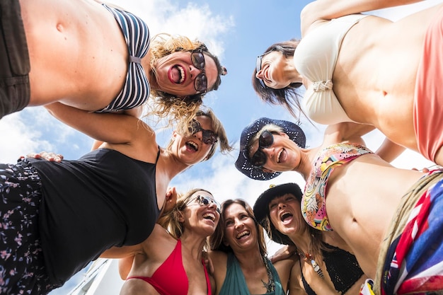 Ritratto a basso angolo di amici felici che indossano bikini urlando mentre stanno in piedi contro il cielo