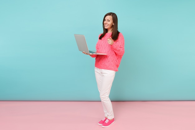 Ritratto a figura intera di donna in maglione rosa lavorato a maglia, pantaloni bianchi che utilizza computer pc portatile laptop