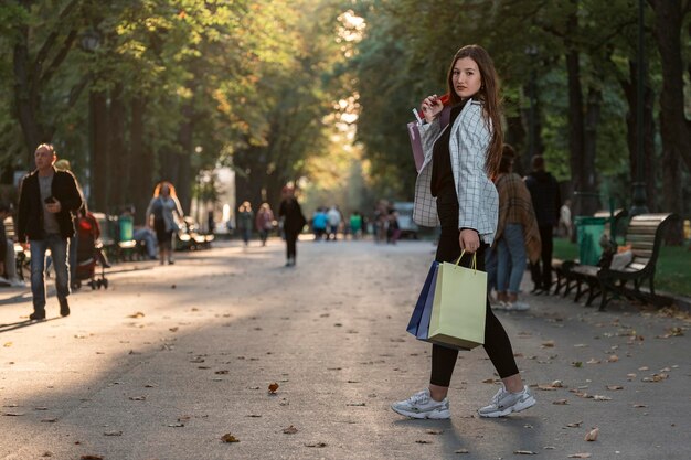 Ritratto a figura intera di giovane donna con borse della spesa di carta che camminano nel parco Cliente felice