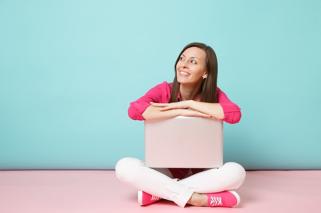 Ritratto a figura intera di giovane donna in camicia rosa camicetta pantaloni bianchi seduta sul pavimento utilizzando un pc portatile