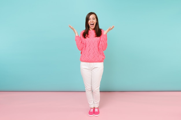 Ritratto a figura intera di giovane donna sorridente in maglione rosa lavorato a maglia, pantaloni bianchi in posa