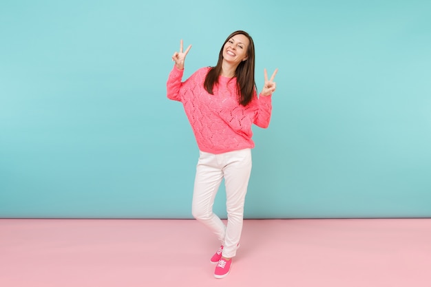 Ritratto a figura intera di giovane donna sorridente in maglione rosa lavorato a maglia, pantaloni bianchi in posa