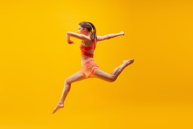 Ritratto a figura intera di giovane ragazza sportiva in movimento isolato su sfondo giallo brillante moderno