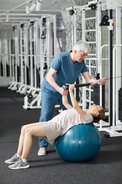 Ritratto a figura intera di terapista riabilitativo senior che lavora con una paziente in palestra in clinica