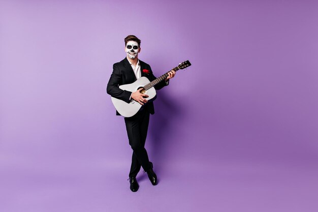Ritratto a figura intera di un gioioso uomo zombie con chitarra bianca Mariachi morti che cantano ad Halloween