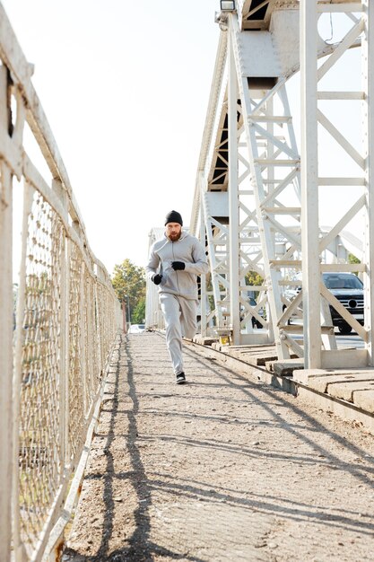 Ritratto a figura intera di un giovane sportivo concentrato che fa jogging sul ponte all'aperto