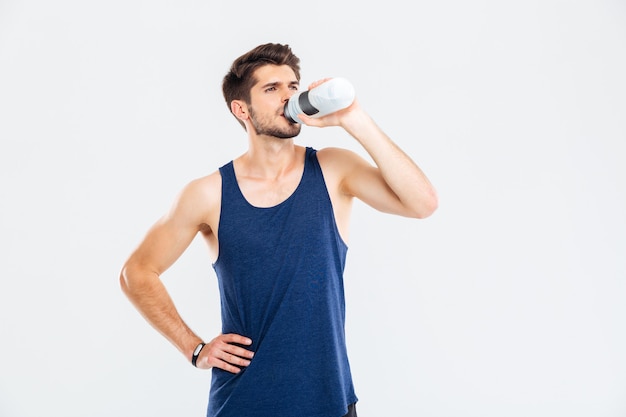 Ritratto a figura intera di un uomo di forma fisica che beve acqua isolata sullo sfondo grigio