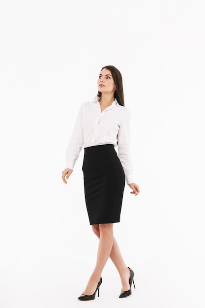 Ritratto a figura intera di una giovane donna d'affari attraente che indossa abiti formali che cammina isolata su un muro bianco