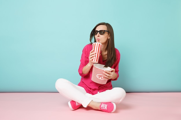 Ritratto a figura intera divertente donna in camicia rosa, pantaloni bianchi seduta sul pavimento a guardare film