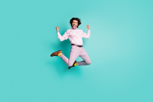 Ritratto a grandezza naturale di un uomo pazzo felice che urla sì salta vestito formale calzini gialli alzano i pugni isolati su sfondo di colore turchese