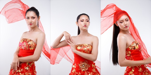 Ritratto a metà corpo di una donna asiatica degli anni '20, lunghi capelli lisci e neri, indossa un costume tradizionale cinese in oro rosso. La ragazza posa su sfondo bianco isolato