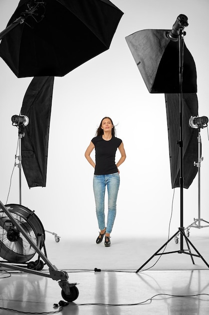 Ritratto a tutta lunghezza di una donna con le luci dell'ombrello in piedi contro uno sfondo bianco in studio