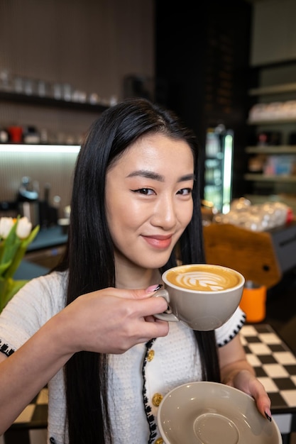 Ritratto a vita di una signora sorridente che tiene una tazza di cappuccino in ceramica nella caffetteria