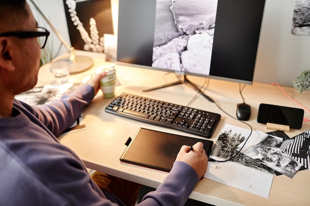 Ritratto ad alto angolo del creatore maschio che modifica fotografie sul posto di lavoro dell'ufficio a casa e utilizza la tabella della penna