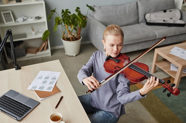 Ritratto ad alto angolo di giovane donna bionda che suona il violino a casa o si esercita nella copia dello studio musicale