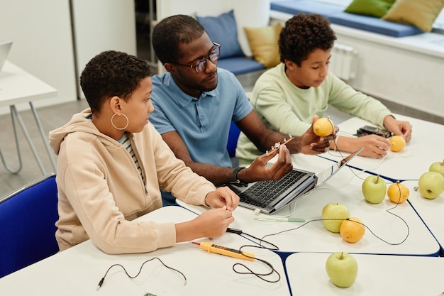 Ritratto ad alto angolo di giovane insegnante afroamericano che lavora su esperimenti scientifici con diversi gruppi di bambini