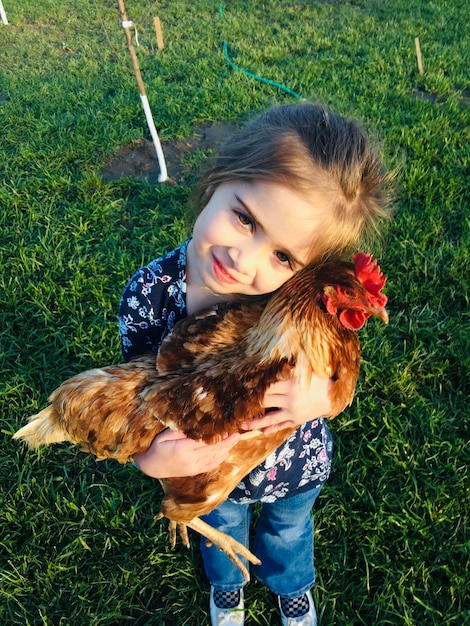 Ritratto ad alto angolo di una ragazza carina che tiene in mano una gallina mentre è in piedi sull'erba