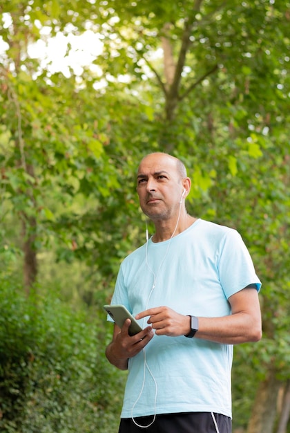 Ritratto ad angolo basso di un uomo più anziano nel parco pensieroso e guardando l'orizzonte mentre ascolta la musica