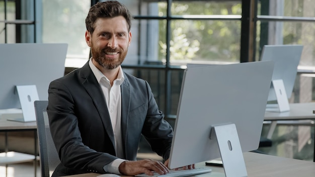 Ritratto adulto barbuto lavoratore freelance uomo in ufficio lavorando laptop digitando sorridere alla telecamera