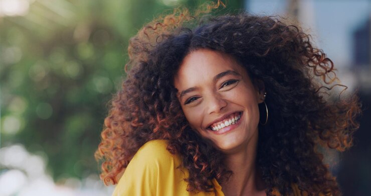 Foto ritratto afro e sorriso con donna all'aperto in città per pendolare o viaggiare come pedone sul marciapiede capelli del viso e felice con persona femminile sicura in città urbana per energia divertimento o benessere
