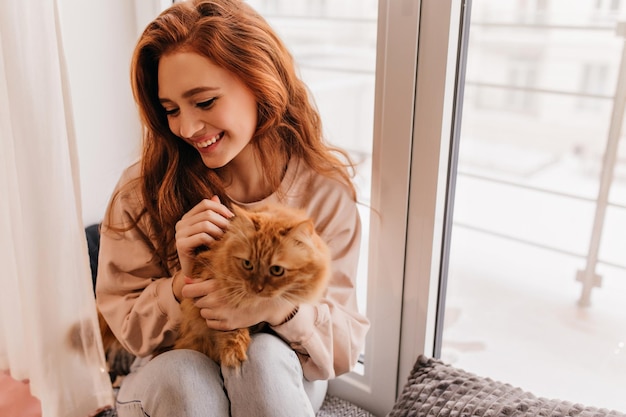 Ritratto al coperto di una bella donna bianca in posa con il suo animale domestico Bella ragazza allo zenzero che si gode il servizio fotografico con il gatto