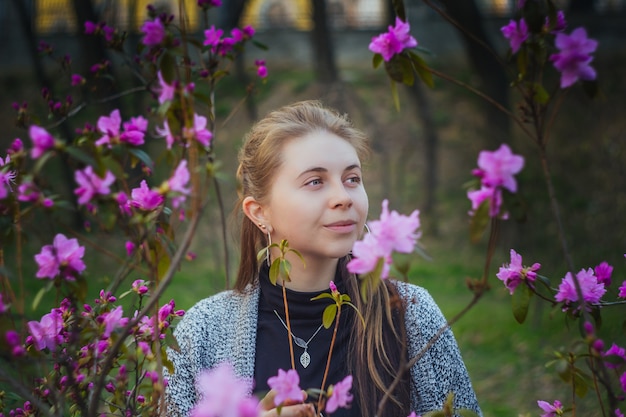 Ritratto all'aperto della donna europea in un cespuglio dei fiori rosa e porpora nel parco di primavera