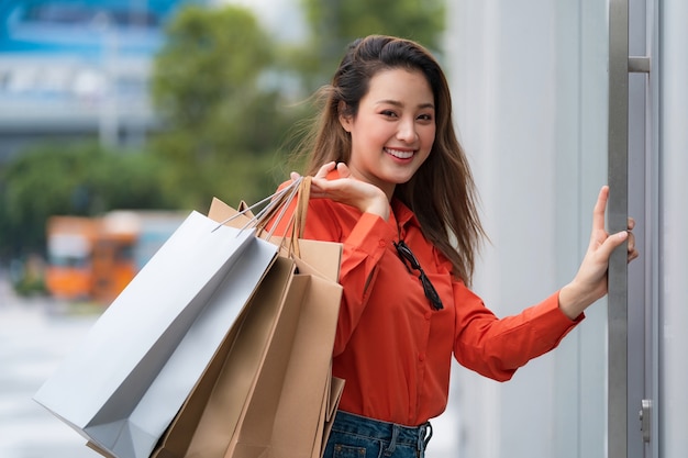 Ritratto all'aperto della donna felice che tiene i sacchetti della spesa e del volto sorridente al centro commerciale