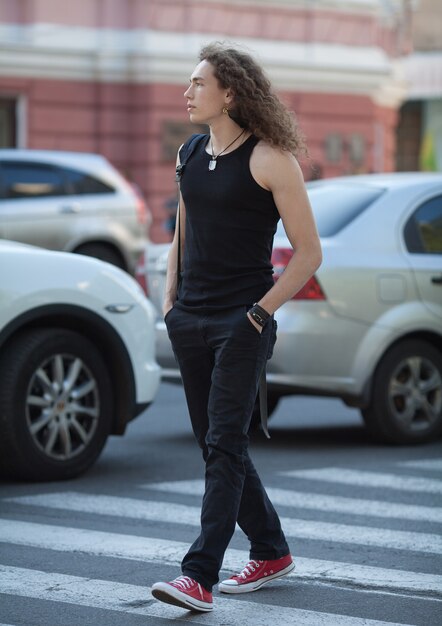 Ritratto all'aperto della via moderna della camminata del giovane. Uomo con lunghi capelli ricci.