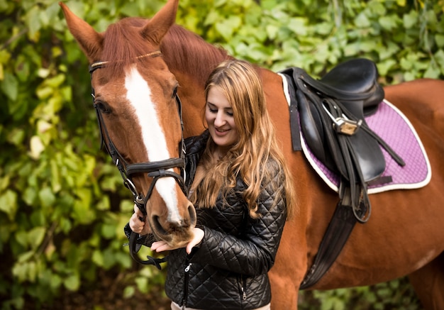 Ritratto all'aperto di bella donna che alimenta il cavallo marrone dalla mano