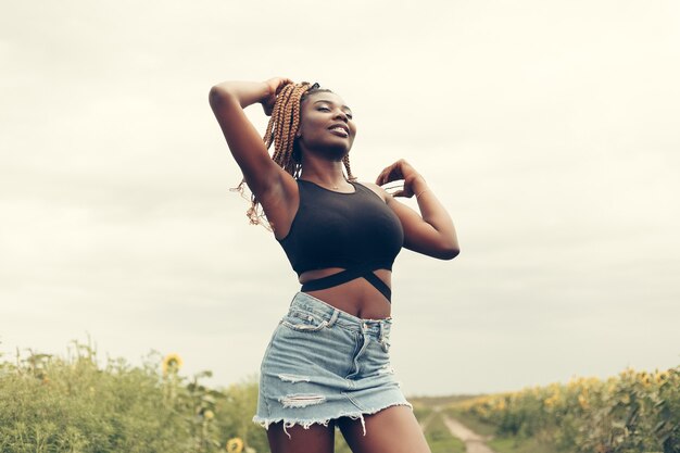 Ritratto all'aperto di bella felice razza mista afroamericana ragazza adolescente femmina giovane donna in un campo di fiori gialli al tramonto dorato del sole della sera