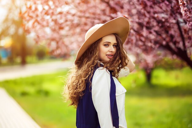 Ritratto all'aperto di giovane bella signora alla moda che posa vicino all'albero di fioritura.