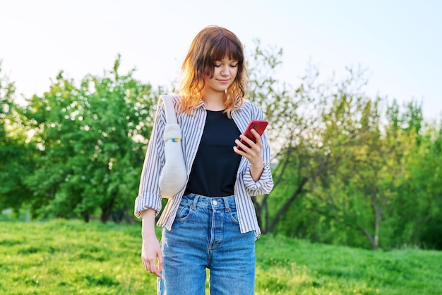 Ritratto all'aperto di giovane ragazza dai capelli rossi alla moda con lo smartphone in mano