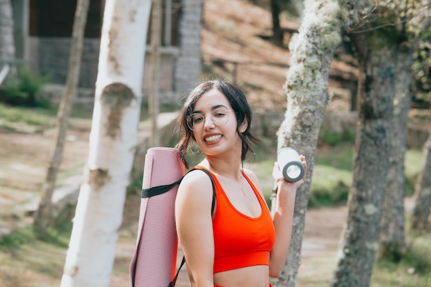 Ritratto all'aperto di hobby di yoga della donna araba che sorride alla macchina fotografica all'aperto nella mattina nel parco vicino a un lago. Copia le immagini dello spazio, allungando e facendo posizioni yoga. Panni sportivi durante una giornata di sole.